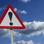 Warning sign with exclamation mark against sky