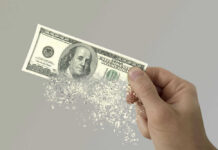 Hand holding a disintegrating hundred dollar bill.