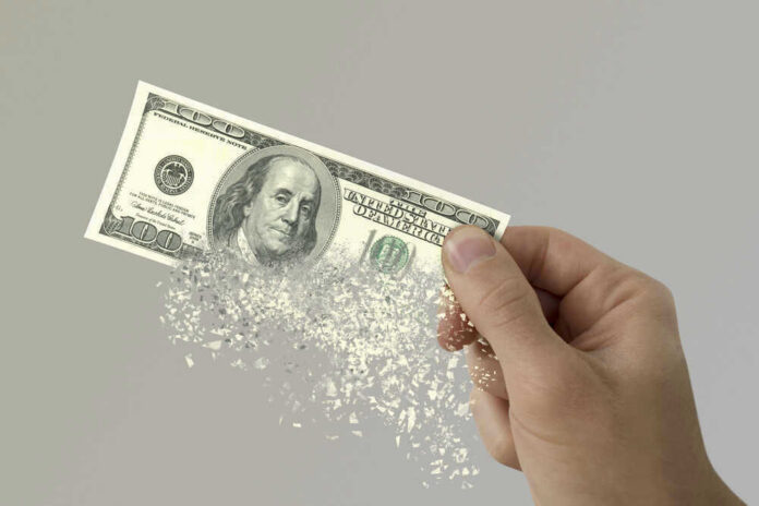 Hand holding a disintegrating hundred dollar bill.