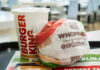 A Whopper Jr. burger wrapped in paper next to a Burger King drink