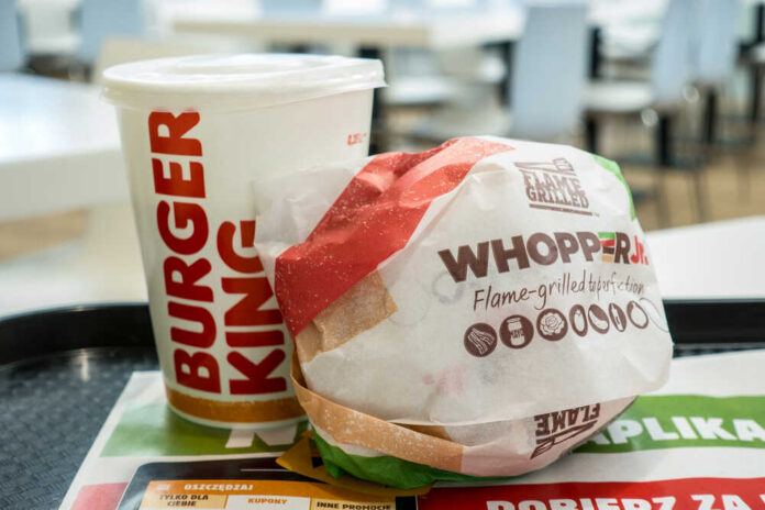 A Whopper Jr. burger wrapped in paper next to a Burger King drink