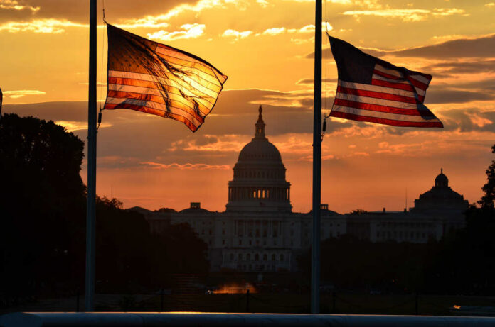 Silhouetted American flags in front of the Capitol building during sunset