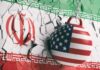 A wrecking ball painted with the American flag is breaking through a wall featuring the Iranian flag
