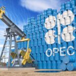 Oil pump jack in front of stacked blue barrels with OPEC logo