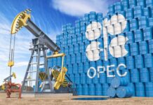 Oil pump jack in front of stacked blue barrels with OPEC logo