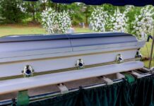 A casket at a graveside surrounded by floral arrangements