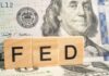Wooden blocks spelling 'FED' in front of a hundred dollar bill