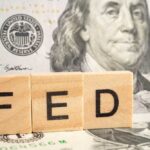 Wooden blocks spelling 'FED' in front of a hundred dollar bill