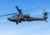 Military Apache helicopter flying against a blue sky