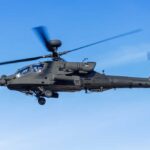 Military Apache helicopter flying against a blue sky