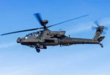 Military Apache helicopter flying against a blue sky