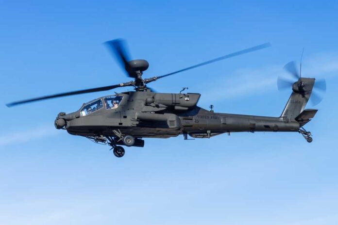 Military Apache helicopter flying against a blue sky