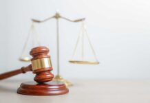 A wooden gavel in front of a balance scale symbolizing justice