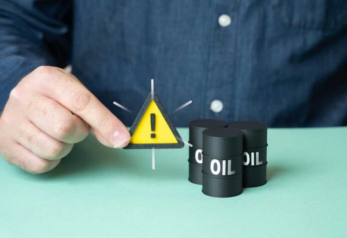 shutterstock_2667717617.jpg A person holding a warning sign next to oil barrels