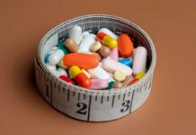 A bowl filled with various colorful pills and capsules next to a measuring tape
