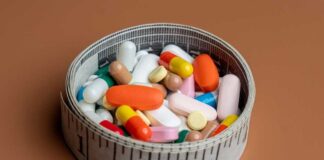 A bowl filled with various colorful pills and capsules next to a measuring tape