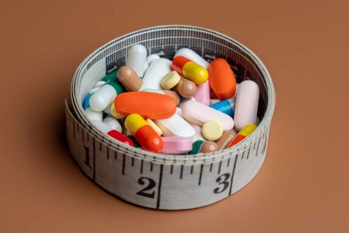 A bowl filled with various colorful pills and capsules next to a measuring tape