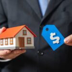 A person in a suit holding a miniature house and a price tag
