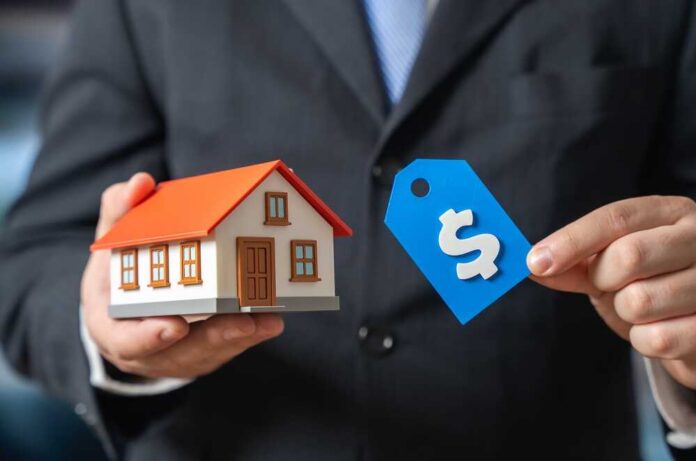 A person in a suit holding a miniature house and a price tag
