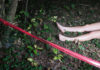 Bare feet visible near caution tape in a wooded area