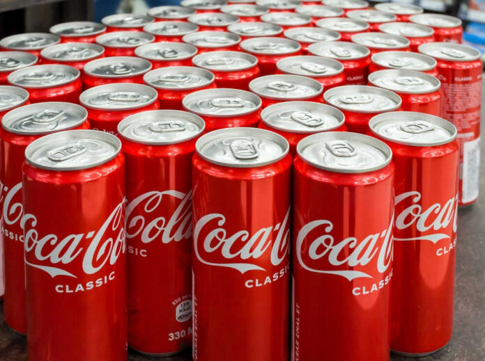 shutterstock_2295132893 Coca-Cola cans stacked on a surface.