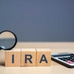 Magnifying glass and wooden blocks spelling 'IRA' next to a calculator