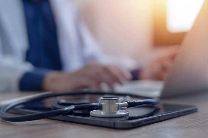 shutterstock_2468694473.jpg Stethoscope and tablet on desk, doctor using laptop.