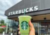 Hand holding a green matcha drink in front of a Starbucks store