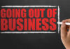 A hand writing 'GOING OUT OF BUSINESS' on a chalkboard