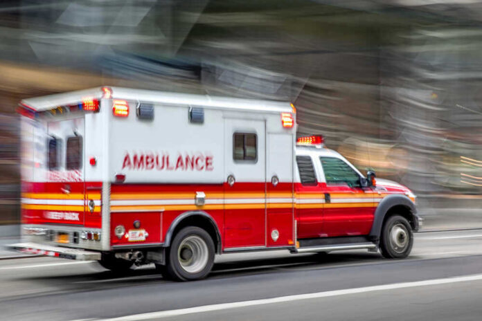 Red and white ambulance driving on a city street.