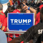People holding Trump 2024 sign at a rally.