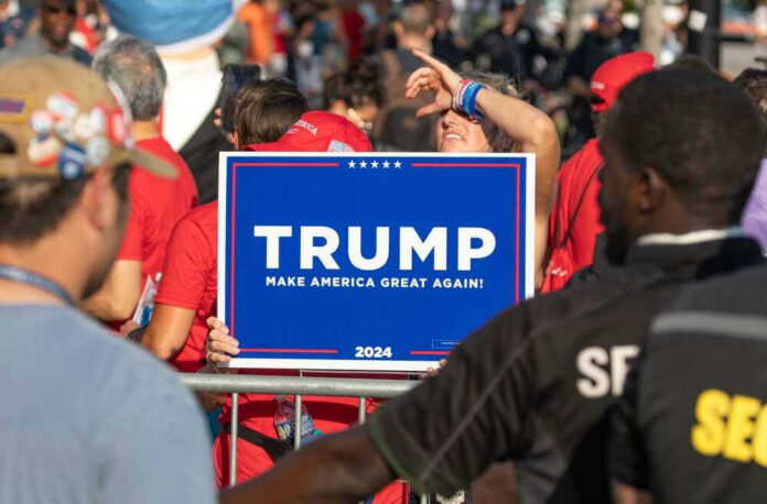 People holding Trump 2024 sign at a rally.
