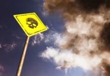 Yellow warning sign with skull symbol under dramatic cloudy sky
