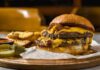 A double cheeseburger with melted cheese and pickles served with potato wedges