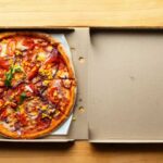 A pizza with various toppings in an open pizza box on a wooden table