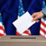 Hand casting a vote into a ballot box.
