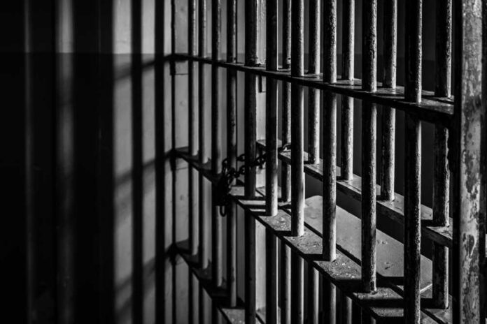 shutterstock_7243457531 Rusty prison bars in dim lighting.