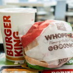 A Whopper Jr. burger wrapped in paper next to a Burger King drink