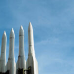 Four white missile launchers pointing upward against a blue sky
