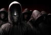 Faceless hooded figures standing in a dark background.