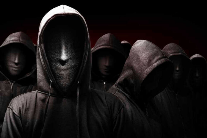 Faceless hooded figures standing in a dark background.