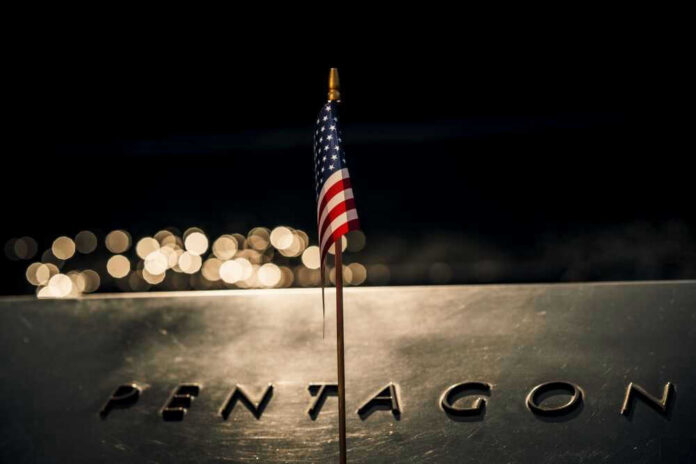 shutterstock_2321355077 American flag above engraved Pentagon sign at night