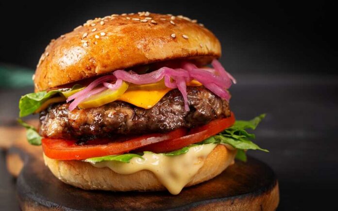 Close-up of a gourmet cheeseburger with lettuce, tomato, and pickled onions