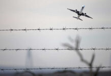 Airplane taking off view through barbed wire fence