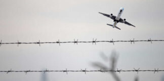 Airplane taking off view through barbed wire fence