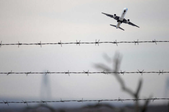 shutterstock_2401451327 Airplane taking off view through barbed wire fence