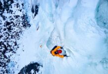 A climber ascending a frozen ice wall in a snowy landscape