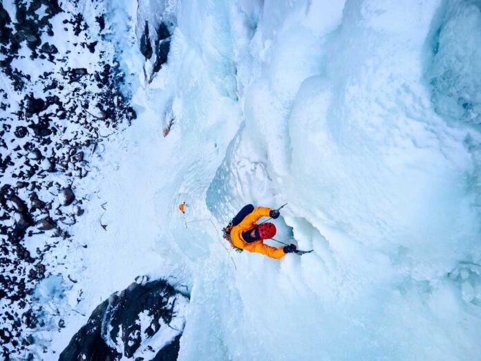 A climber ascending a frozen ice wall in a snowy landscape