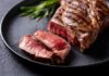 A beautifully grilled steak with a slice cut off, garnished with herbs