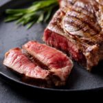 A beautifully grilled steak with a slice cut off, garnished with herbs